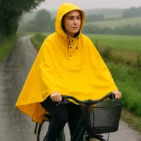 Femme portant la cape de pluie vélo Badawin jaune à vélo à la campagne