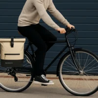 Cycliste roulant à Paris avec le sac Badawin Anna sable fixé sur le porte-bagages, tenue urbaine noire.